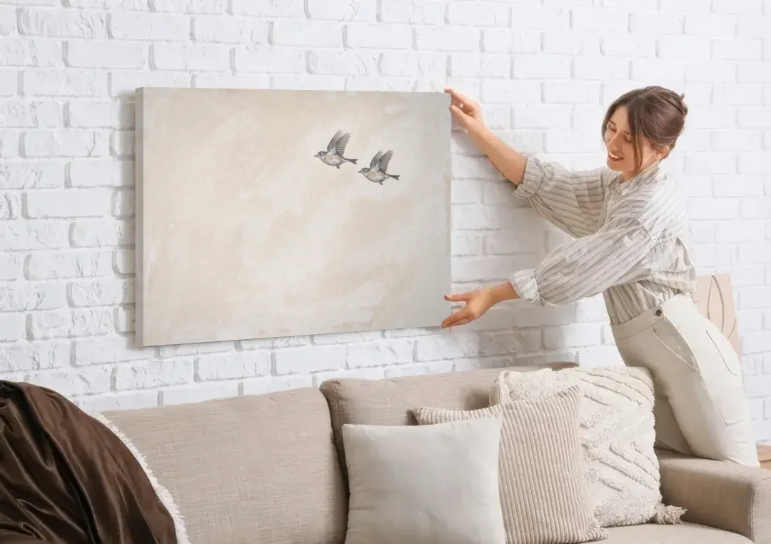 Bird Wall Art of a Pair in Beige Air canvas wall art being hung on a white brick wall above a sofa