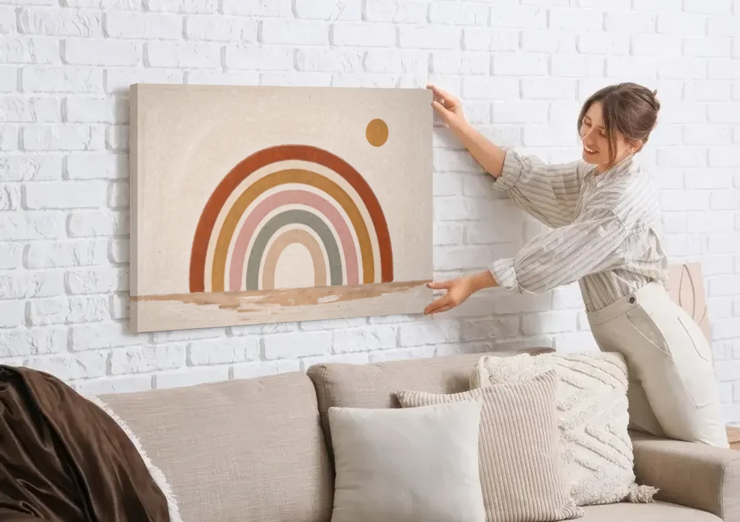 Boho Rainbow Wall Art with a Floating Sun canvas wall art being hung on a white brick wall above a sofa