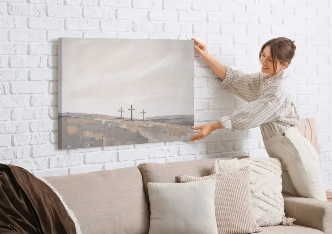 Cross Wall Art of Calvary Under a Quiet Sky canvas wall art being hung on a white brick wall above a sofa