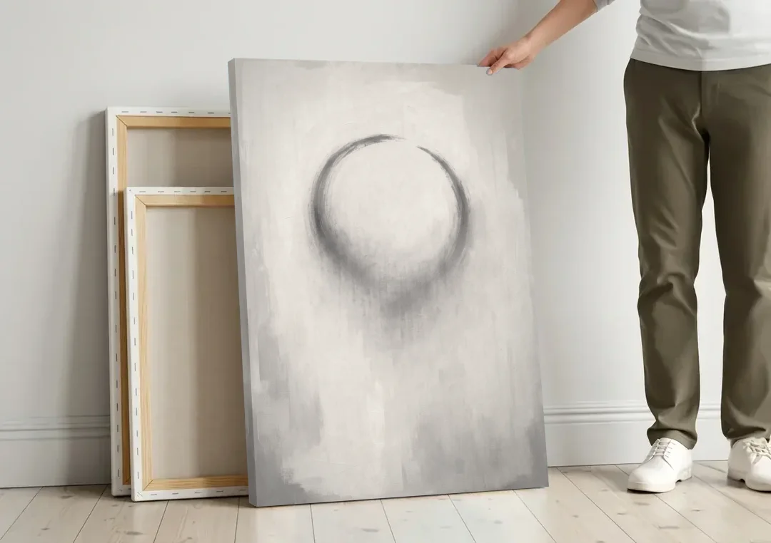 Minimalist Black and White Dissolving Charcoal Circle canvas wall art leaning against a wall next to blank canvases