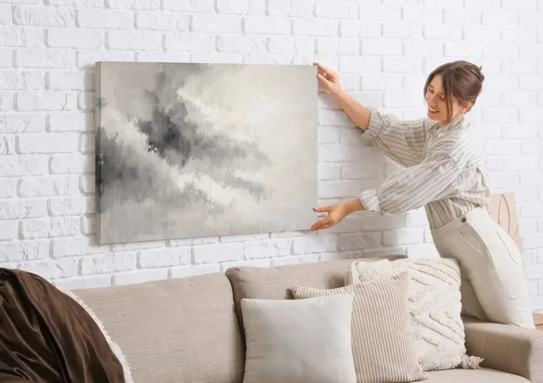 Monochrome Drifting Weather in Soft Gray Wash canvas wall art being hung on a white brick wall above a sofa