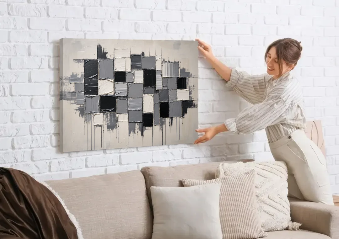 Dripping Grid of Black and Grey Squares canvas wall art being hung on a white brick wall above a sofa