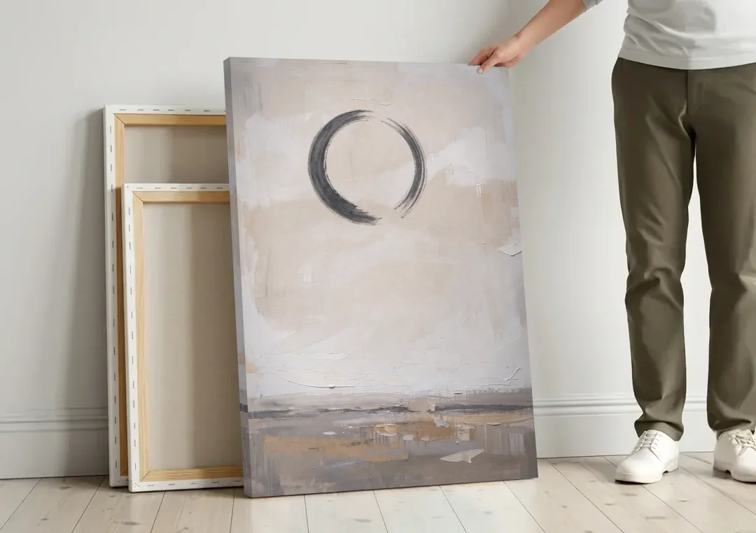 Enso Circle Painting Over Warm Sand canvas wall art leaning against a wall next to blank canvases