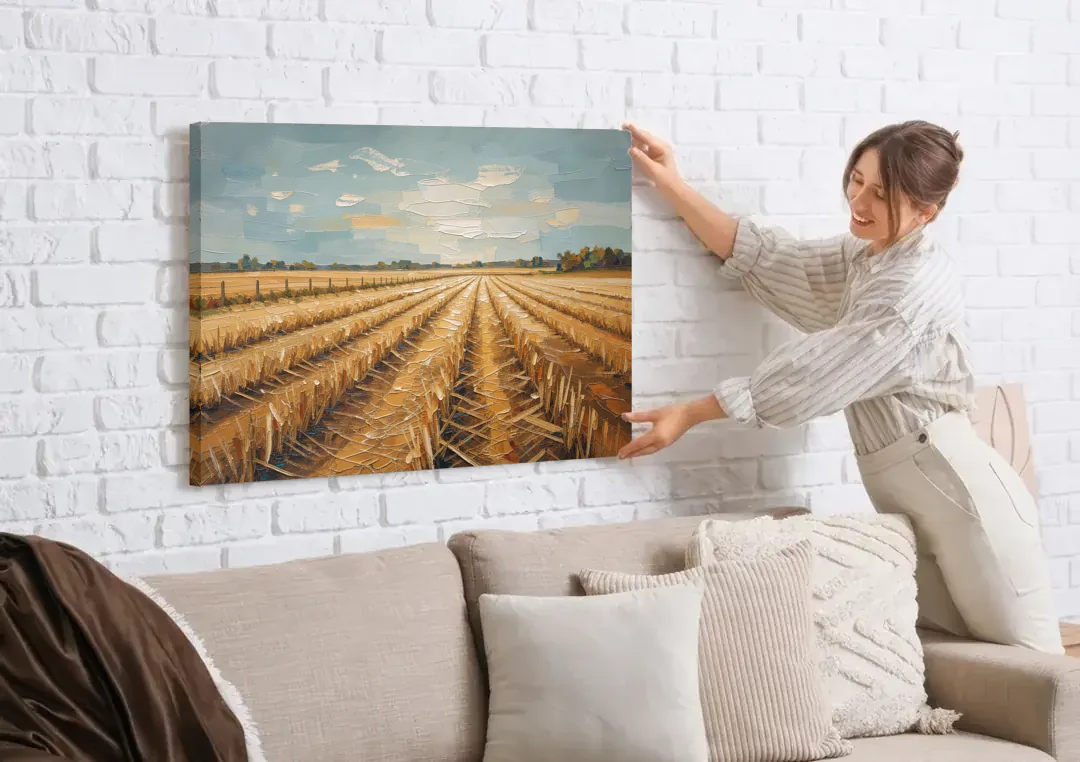 Harvested Stubble Field Rows Under a Pale Sky canvas wall art being hung on a white brick wall above a sofa