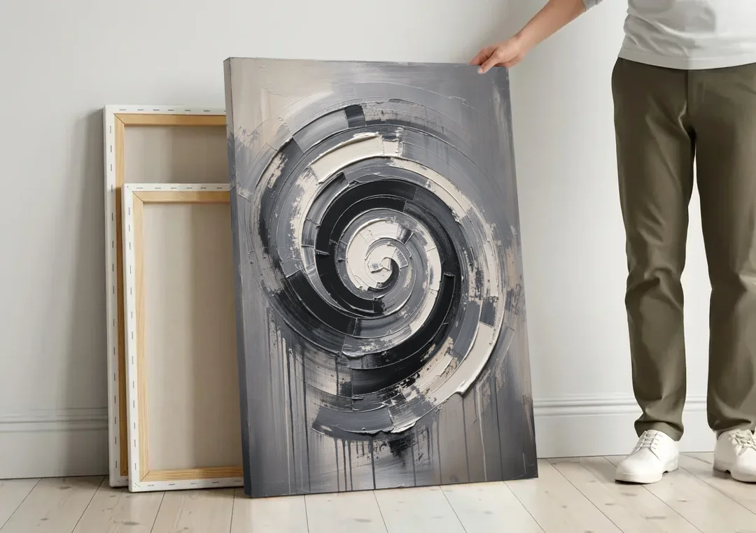 Modern Black and White Inward Spiral canvas wall art leaning against a wall next to blank canvases