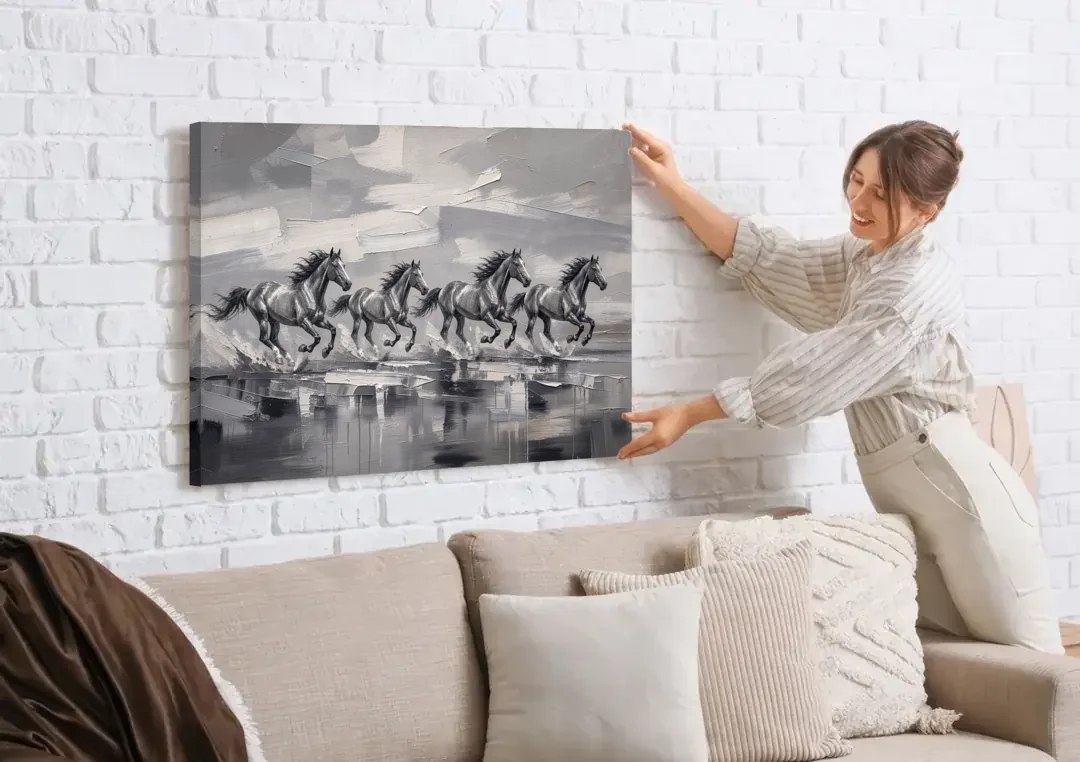 Large Black and White Scene of Four Galloping Horses canvas wall art being hung on a white brick wall above a sofa