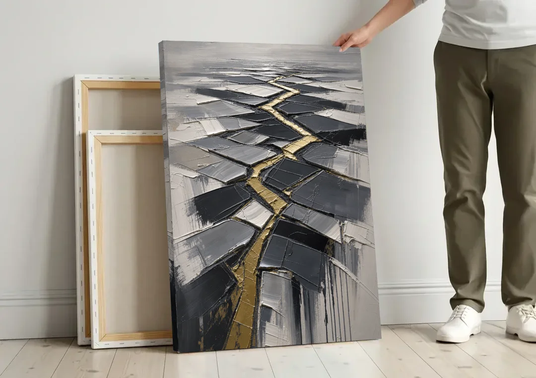 Modern Black White and Gold Abstract Fissure canvas wall art leaning against a wall next to blank canvases