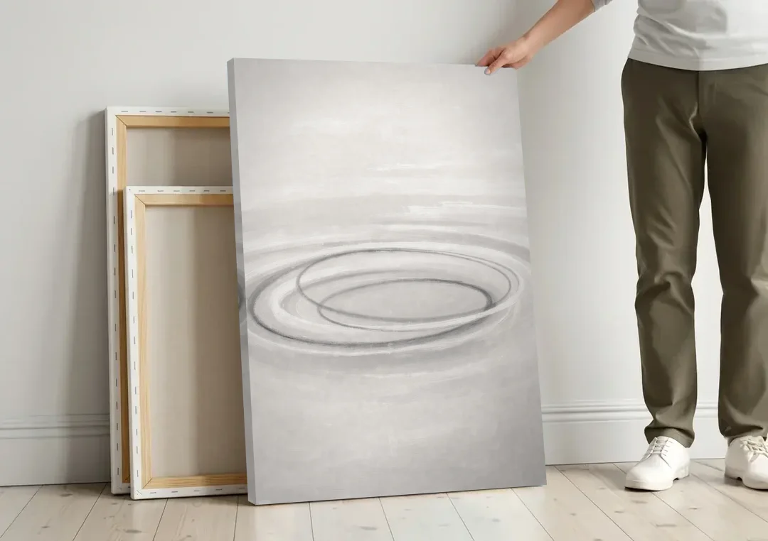 Modern Black White and Grey Abstract Ripple Rings canvas wall art leaning against a wall next to blank canvases
