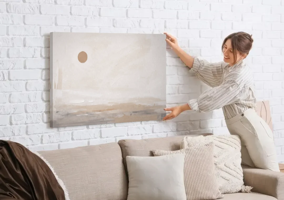 Negative Space Art with a High Clay Sun canvas wall art being hung on a white brick wall above a sofa