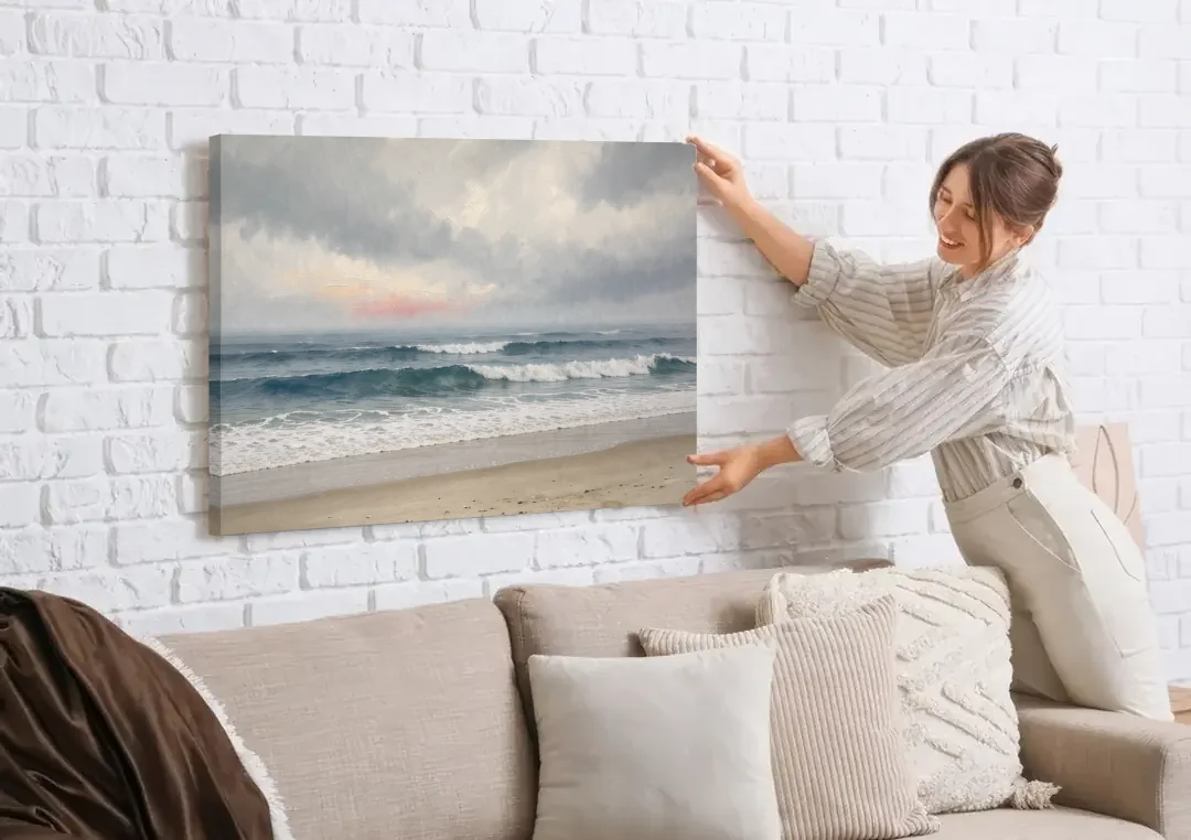 Neutral Coastal Pink Glow Over Gray Surf canvas wall art being hung on a white brick wall above a sofa