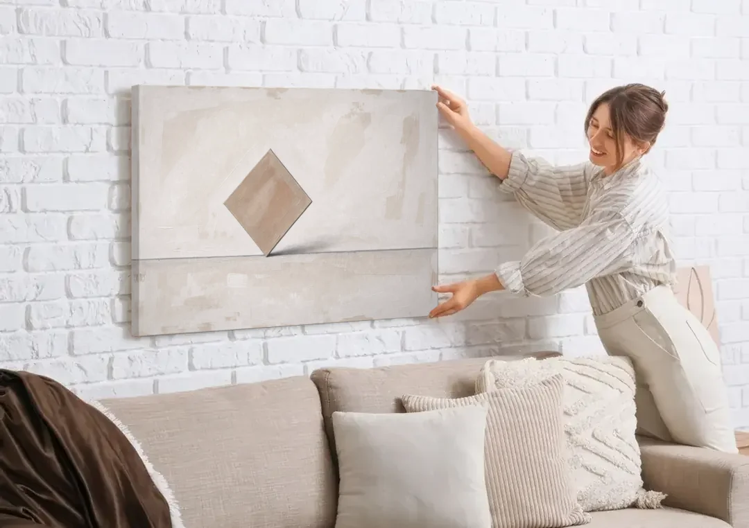 Neutral Modern Wall Art of a Balancing Square canvas wall art being hung on a white brick wall above a sofa