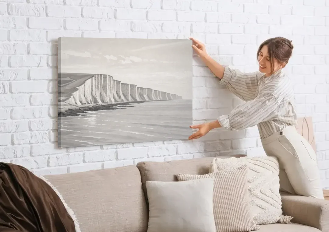 Office Art Prints Chalk Cliffs Above a Calm Sea canvas wall art being hung on a white brick wall above a sofa