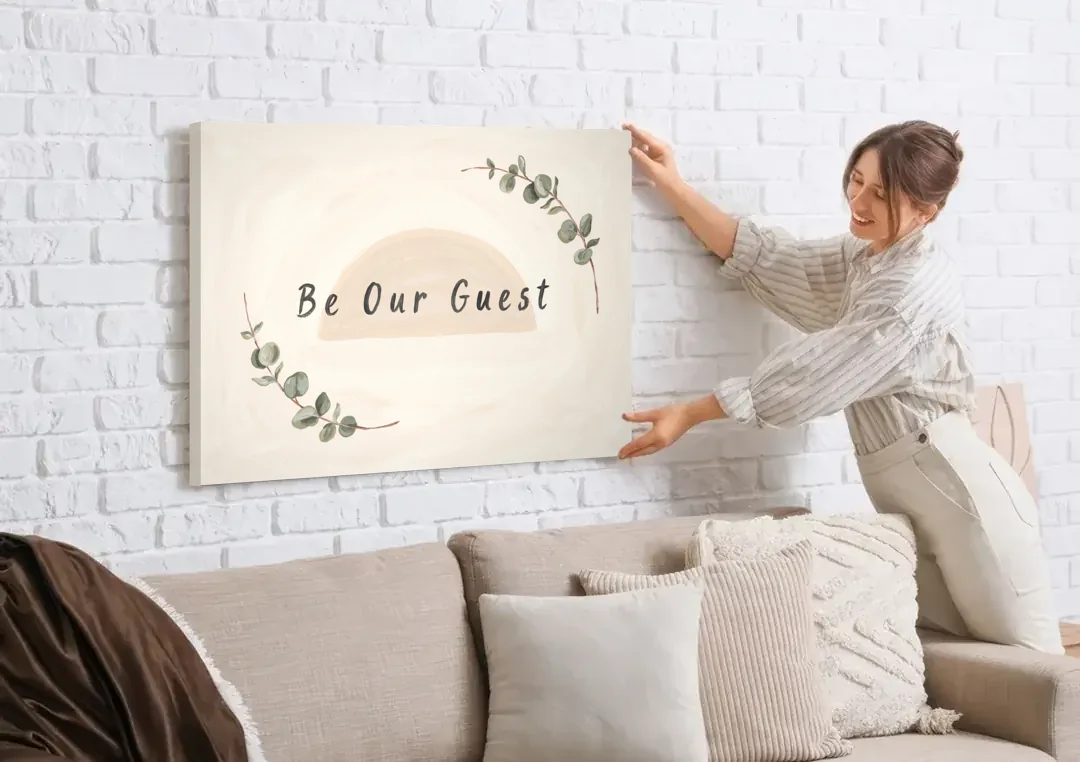 Over the Bed Wall Art Be Our Guest Eucalyptus canvas wall art being hung on a white brick wall above a sofa