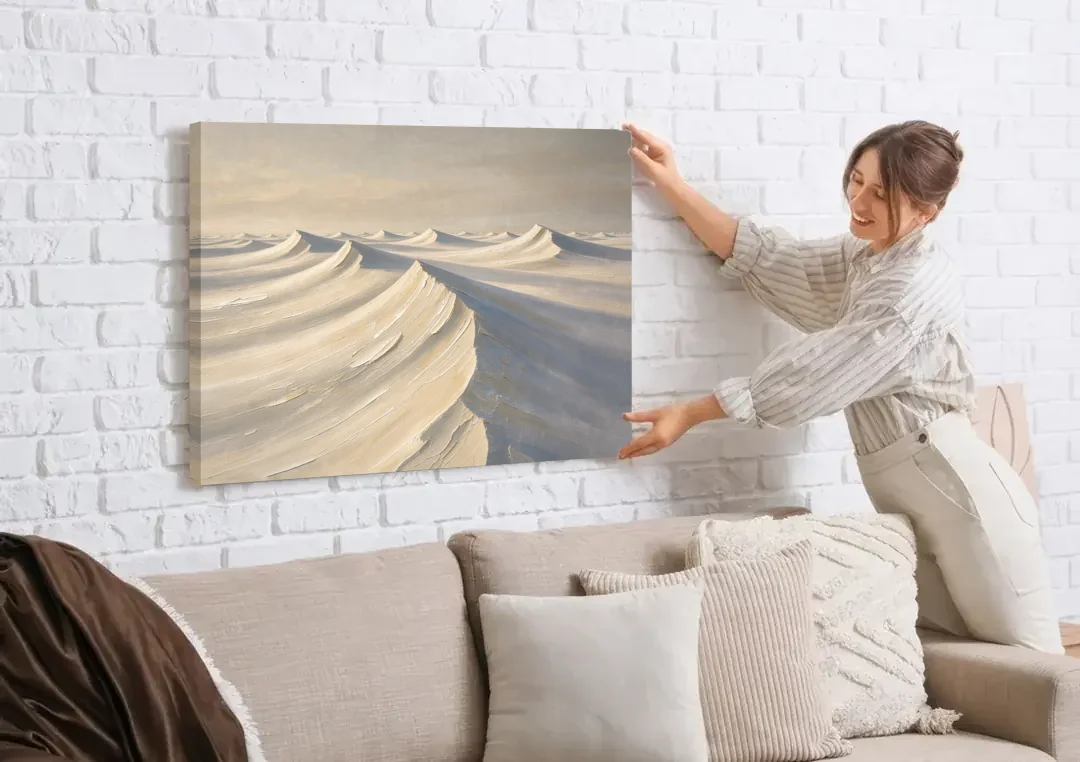Oversized Neutral Wall Art of Curling Snow Drifts canvas wall art being hung on a white brick wall above a sofa