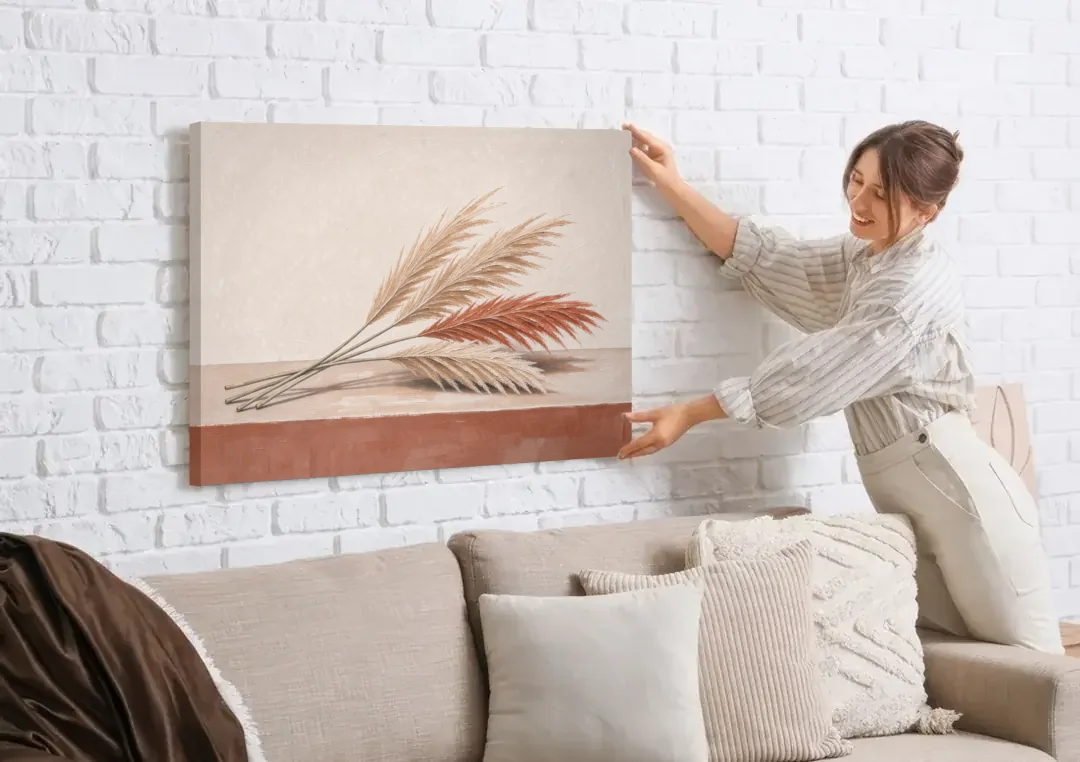 Pampas Grass Wall Art with Three Resting Plumes canvas wall art being hung on a white brick wall above a sofa