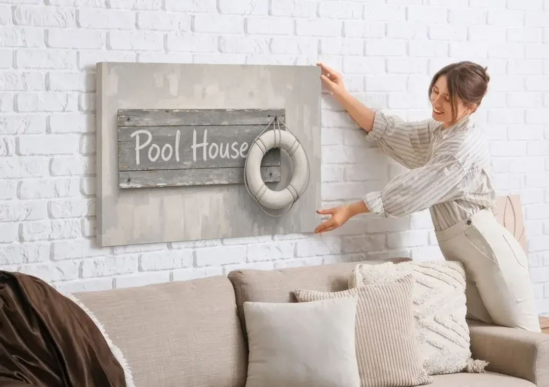 Pool House Sign with White Life Ring canvas wall art being hung on a white brick wall above a sofa