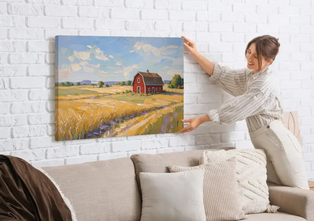 Red Barn Across Golden Grain Fields canvas wall art being hung on a white brick wall above a sofa
