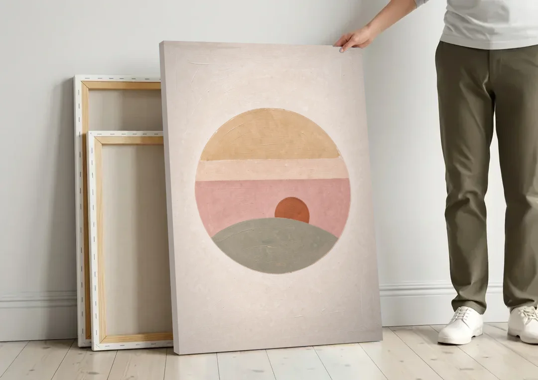 Round Window Landscape with Low Rust Sun canvas wall art leaning against a wall next to blank canvases