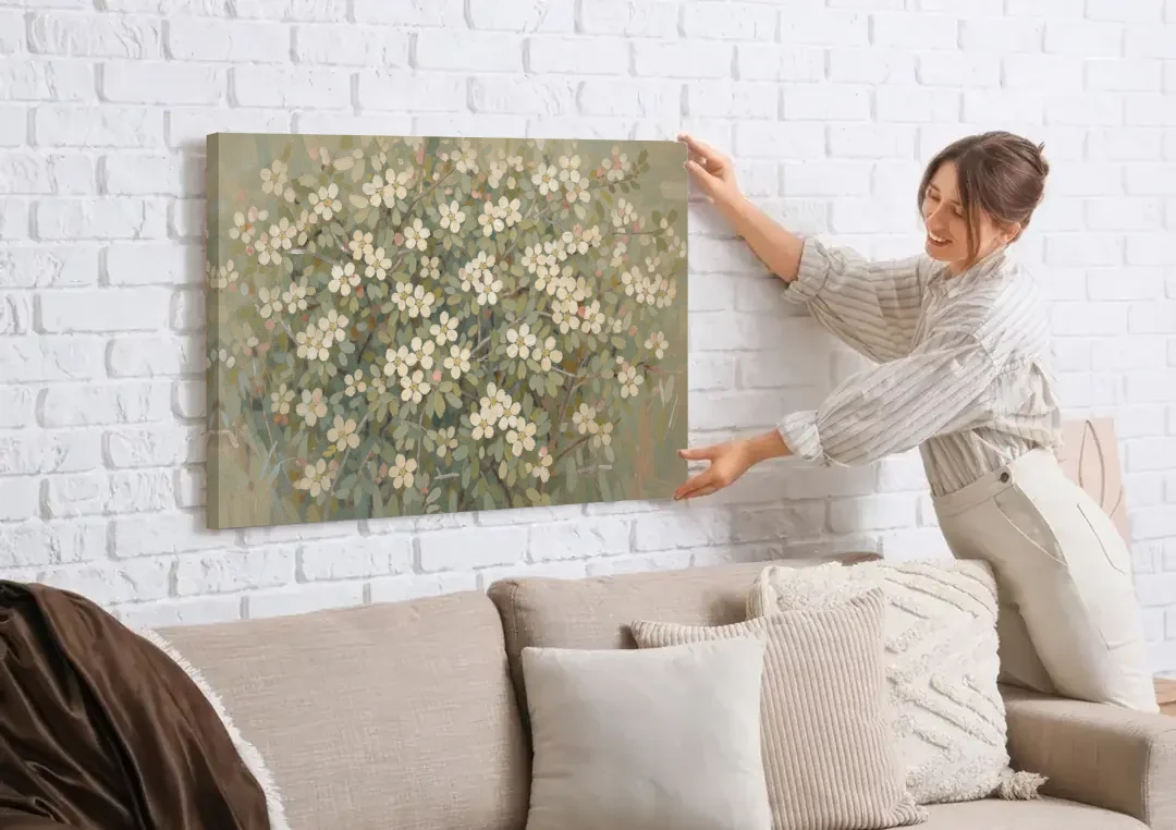 Sage Green Botanical Wall Art of Hedgerow Blossoms canvas wall art being hung on a white brick wall above a sofa