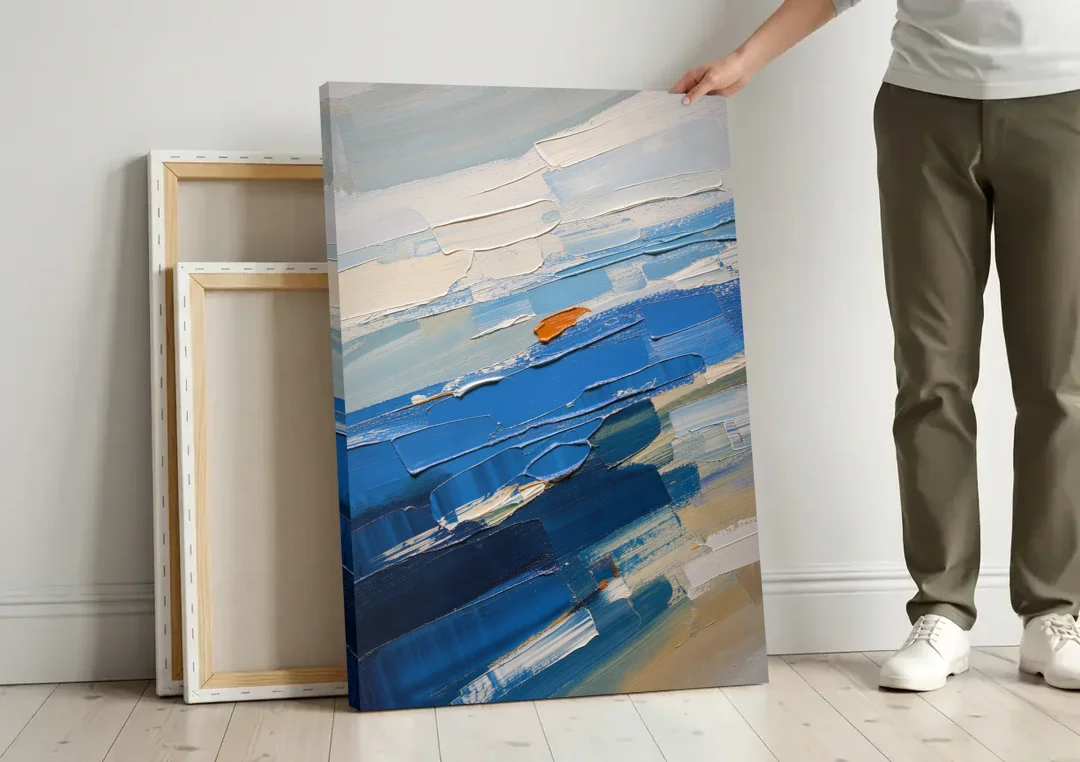 Set of Three Abstract Prints Blue Strata Triptych II canvas wall art leaning against a wall next to blank canvases