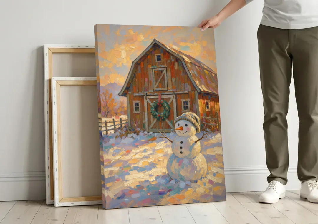 Snowman by the Red Barn with Wreath canvas wall art leaning against a wall next to blank canvases