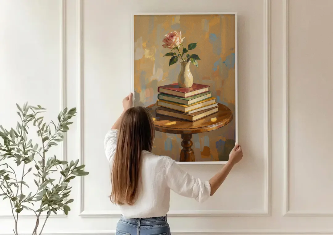 Stack of Books Painting with a Blush Rose canvas wall art being hung on a paneled wall