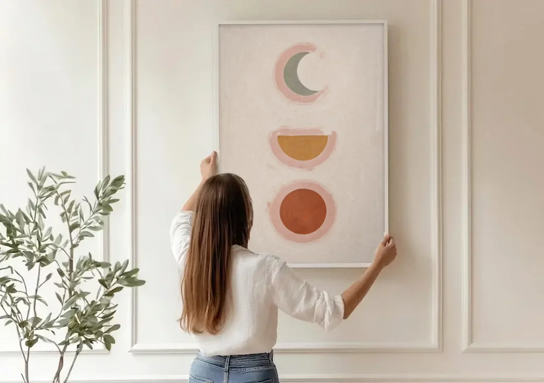 Three Moon Phases Stacked in Earth Tones canvas wall art being hung on a paneled wall