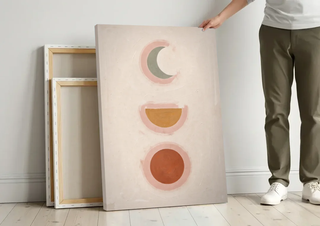 Three Moon Phases Stacked in Earth Tones canvas wall art leaning against a wall next to blank canvases
