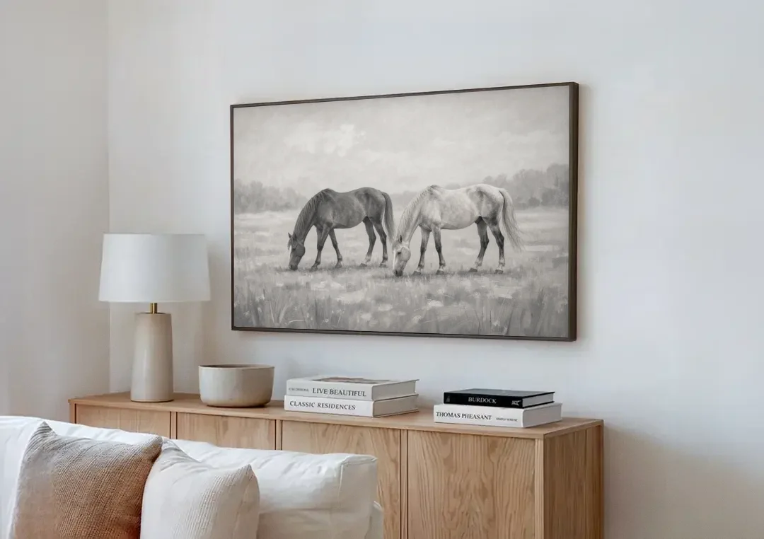 Two Horses Grazing in Misty Pasture in Black and White canvas wall art above a wooden sideboard next to a sofa