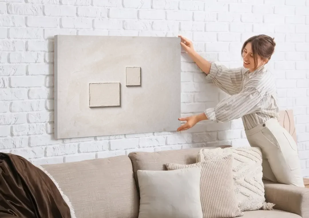 Two Offset Off-White Relief Blocks on Plaster canvas wall art being hung on a white brick wall above a sofa