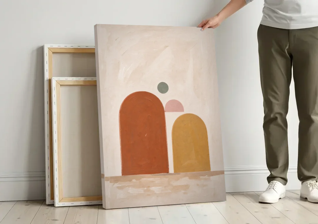 Two Uneven Arches with a Pink Half Sun canvas wall art leaning against a wall next to blank canvases