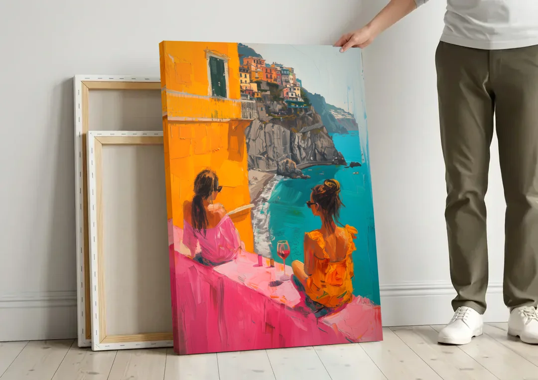 Two Women Painting by the Sea canvas wall art leaning against a wall next to blank canvases
