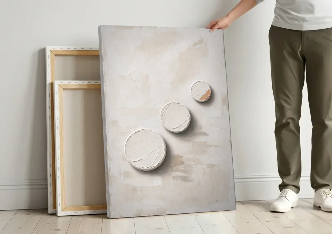 White Textured Wall Art of Three Rising Discs canvas wall art leaning against a wall next to blank canvases